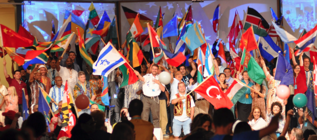 People waving various international flags indoors.