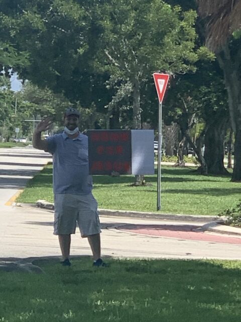 Man holding sign on sidewalk near road.