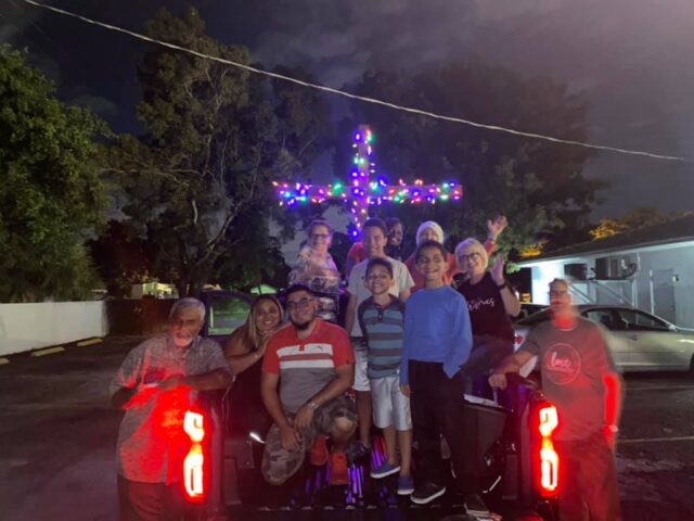 Group celebrating with illuminated cross on truck.