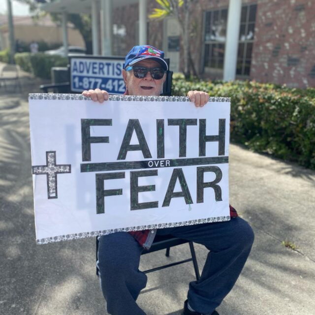 Person holding "Faith Over Fear" sign outside.