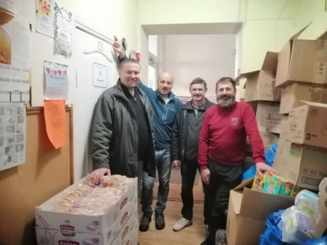Four men standing in a storage room.