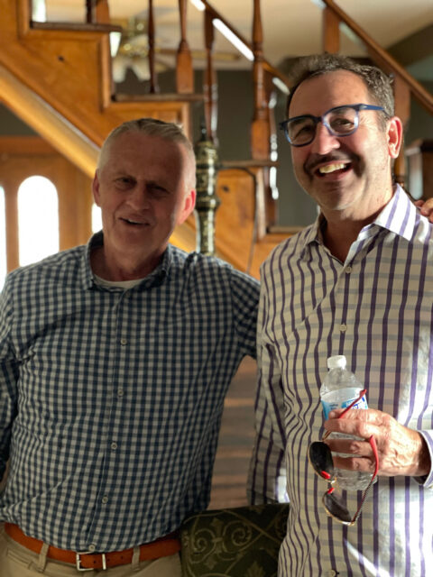 Two men smiling indoors, holding water bottle.