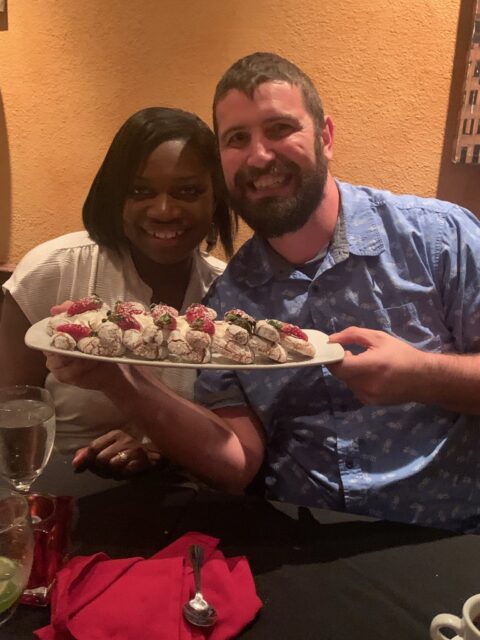 Couple smiling with dessert platter at restaurant.