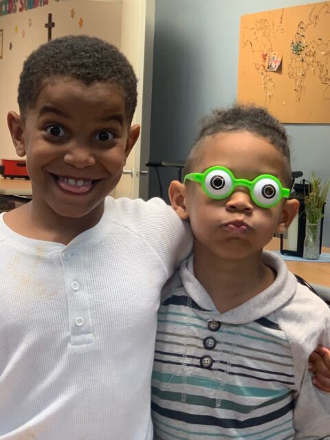 Two kids smiling, one wearing funny glasses.
