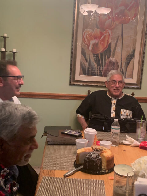 Three men dining with cake on table.