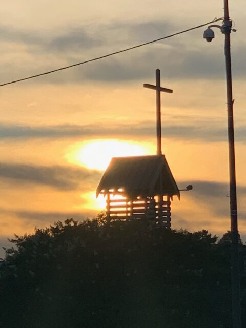 Sunset behind cross on wooden structure.
