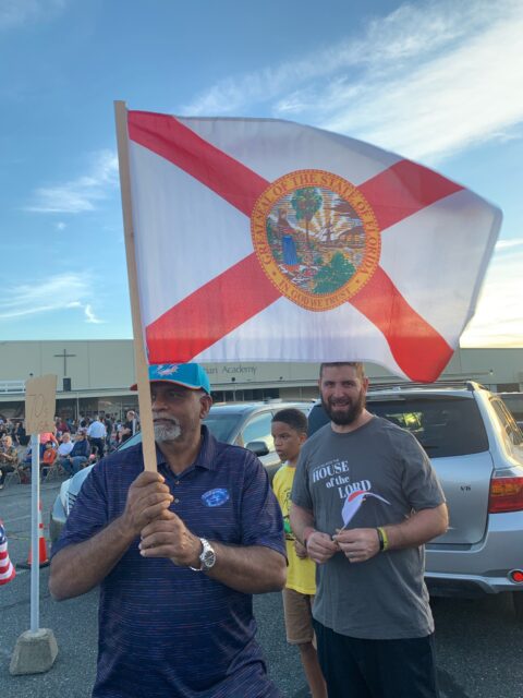 Man holding Florida flag at outdoor gathering.