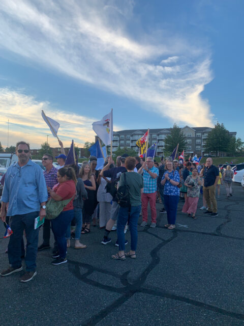 Crowd gathered with flags in parking lot.