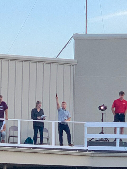 Person holding a microphone on rooftop stage.