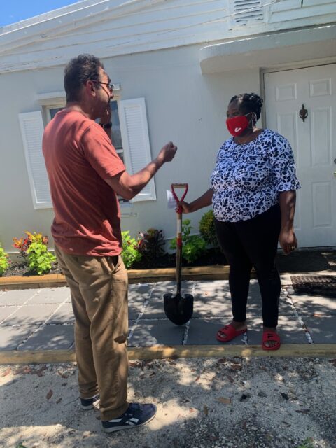Two people talking outside with a shovel.