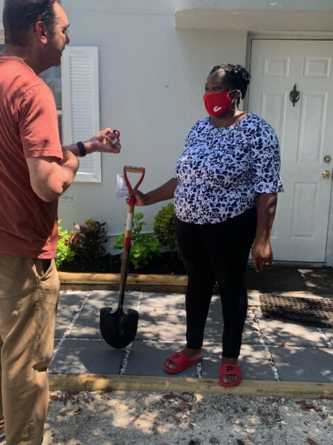 Two people talking outside with a shovel.