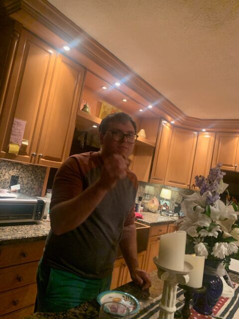 Man standing in kitchen holding a snack.