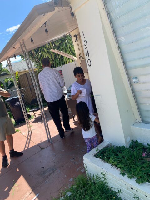 Children outside house with adults nearby.