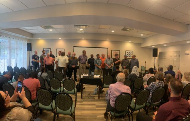 People standing in front of seated audience.