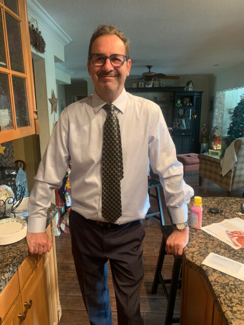 Man standing in kitchen wearing tie, smiling.