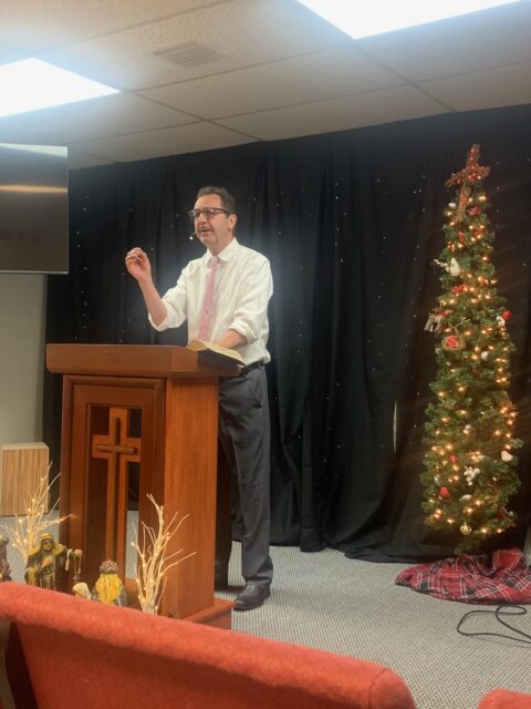 Man speaking at podium near decorated tree.