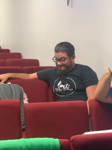 Man sitting in red theater seats, smiling.