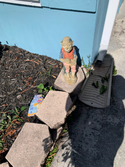 Garden gnome statue beside mulch and bricks.