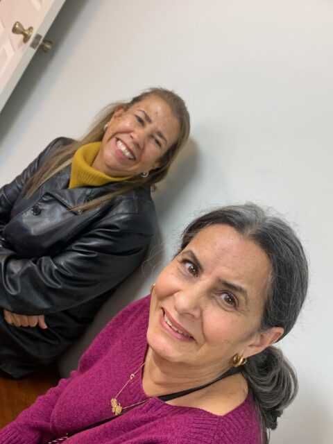 Two smiling women sitting indoors, relaxed atmosphere.