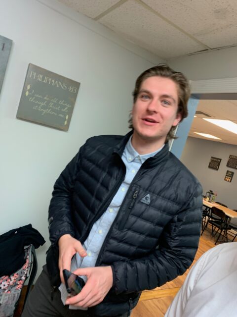 Person smiling indoors, holding a phone.