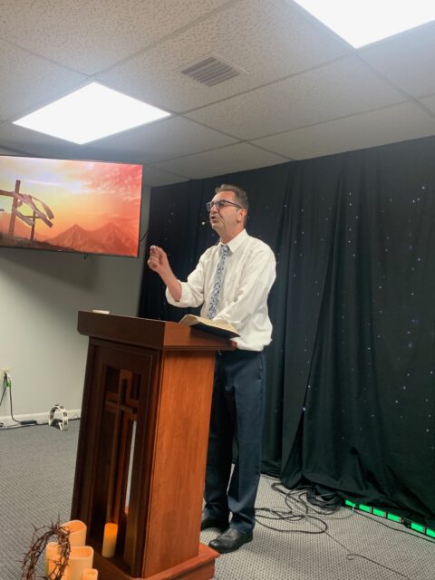 Man speaking at a podium with cross.