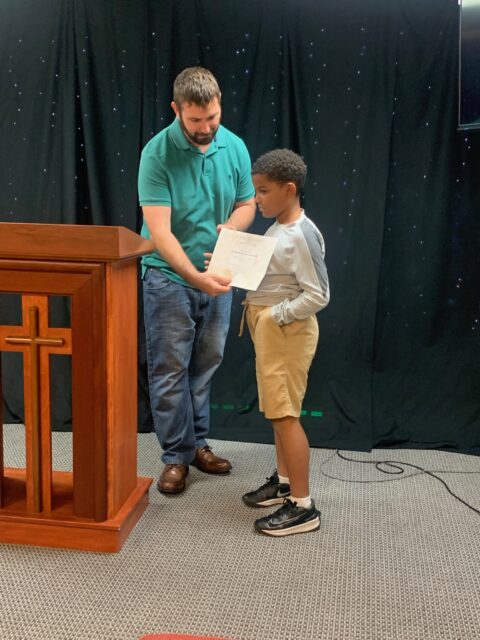 Man presenting certificate to young boy.