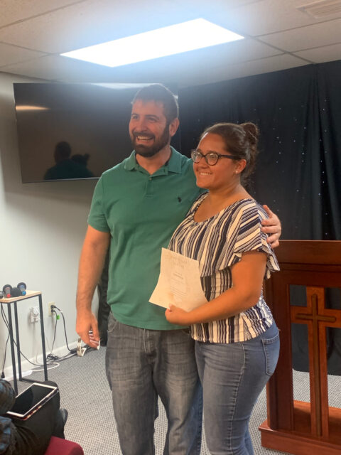 Two people smiling, holding a paper together.