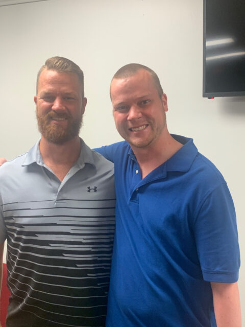 Two smiling men standing together indoors.