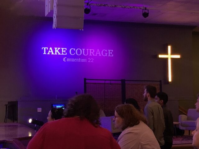 People at event with "Take Courage" sign.