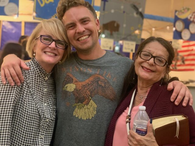 Three people smiling and embracing indoors.