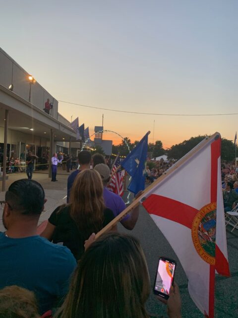 Crowd with flags at outdoor event, sunset.